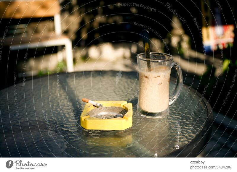 Eiskaffee und Zigarette im gelben Aschenbecher an einem sonnigen Tag trinken Getränk Glas braun Koffein Hintergrund Tisch Nahaufnahme Kaffee kalt Lebensmittel