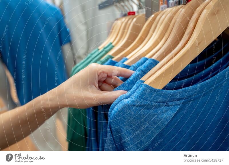 Frau kauft Hemd in Bekleidungsgeschäft. Frau wählt Kleidung. Shirt auf Kleiderbügel hängen auf dem Regal in der Kleidung zu speichern. Mode Einzelhandelsgeschäft im Einkaufszentrum. Kleidung auf Kleiderbügeln in einem Bekleidungsgeschäft.