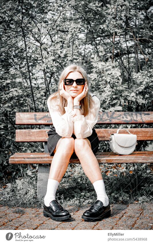 Portrait einer jungen blonden Frau mit Sonnenbrille auf einer Bank im Park. langhaarig feminin weiblich Gesicht natürlich lange Haare attraktiv Schönheit
