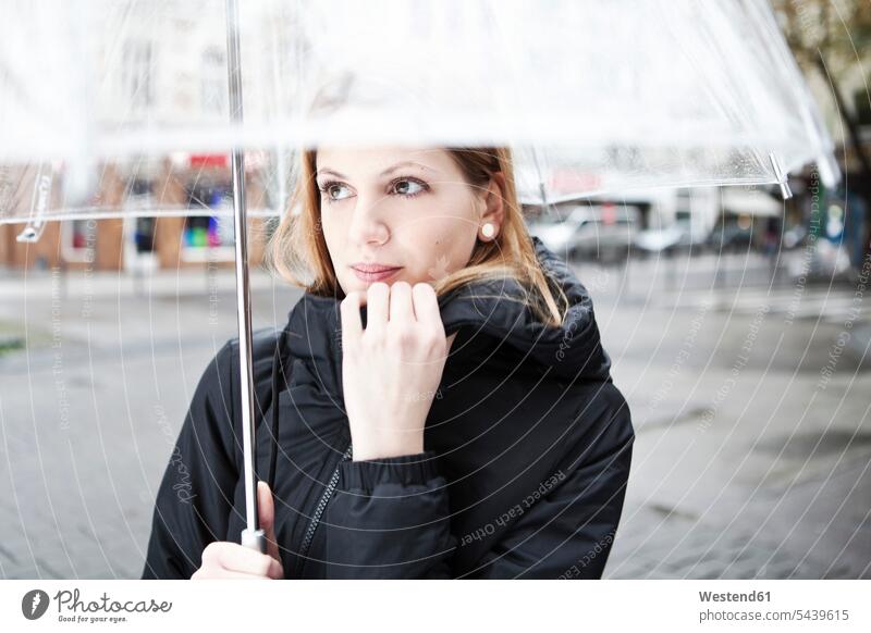 Junge Frau hält durchsichtigen Regenschirm Europäer Kaukasier kaukasisch Europäisch halten haltend festhalten Seitenblick Blick zur Seite Außenaufnahme außen