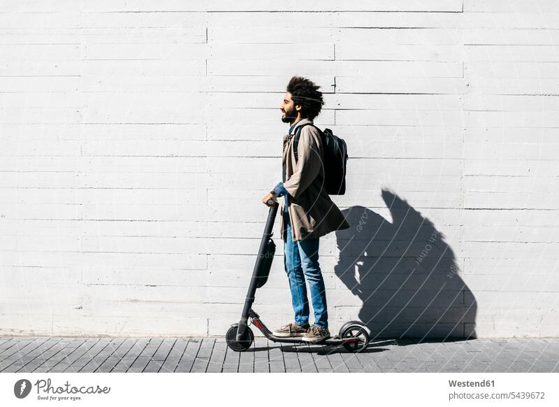 Mann mit Rucksack auf E-Scooter Rucksäcke freuen zufrieden stehend steht Muße mobil außen draußen im Freien staedtisch städtisch Urbanitaet Urbanität Trends