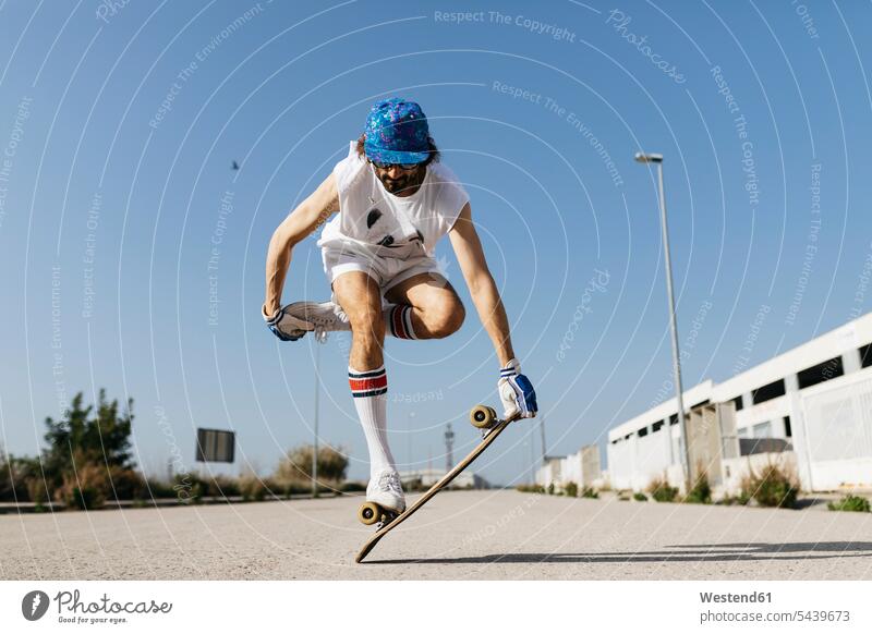Mann in stilvollem sportlichen Outfit steht auf Skateboard gegen blauen Himmel Trick Skateboarder Skateboardfahrer Skateboarders Skater skateboarden Männer