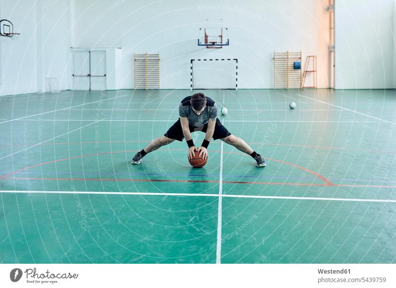 Mann mit Basketball, Beine strecken, Halle Freizeitsport Basketballspieler Basketballer dehnen Dehnübung Stretching Dehnung stretchen Freizeitaktivität Muße