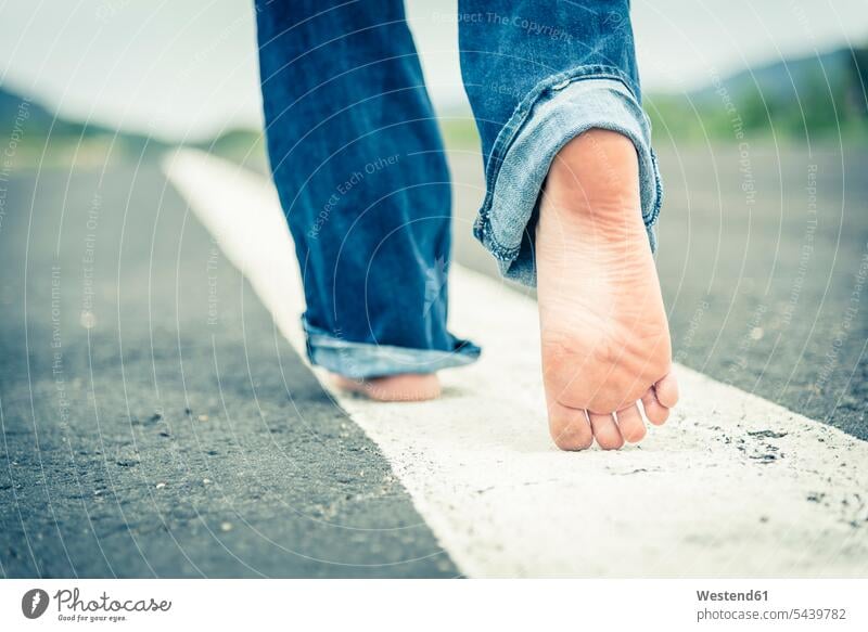 Junge Frau geht barfuss auf der Mittellinie einer leeren Strasse, Teilansicht Europäer Kaukasier kaukasisch Europäisch gehen gehend Textfreiraum Asphalt