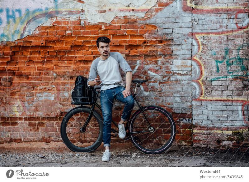 Junger Mann mit Pendler Fixie Fahrrad stehen an Backsteinmauer mit Handy und Kopfhörer Ohrhörer Mobiltelefon Handies Handys Mobiltelefone Backsteinwand