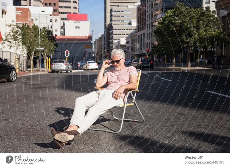 Älterer Mann sitzt auf einem Stuhl auf der Straße und trägt eine Sonnenbrille Stadt staedtisch städtisch Männer männlich Stuehle Stühle Sonnenbrillen Brille