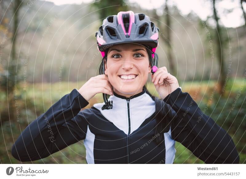 Porträt einer lächelnden Frau, die einen Fahrradhelm aufsetzt aufsetzen Radhelm Fahrradhelme Mountainbiking mountainbiken MTB weiblich Frauen Helm Helme
