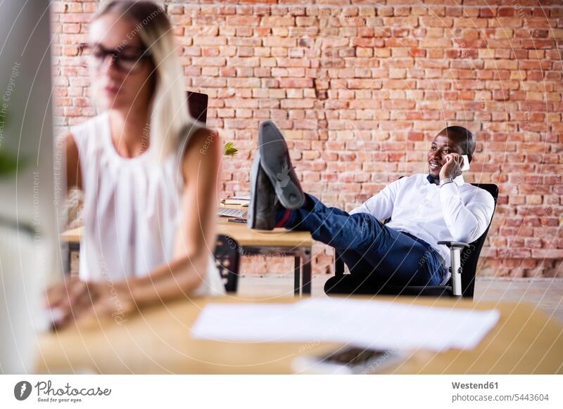 Geschäftsmann am Telefon im Büro mit einem Kollegen, der im Vordergrund arbeitet sitzen sitzend sitzt Businessmann Businessmänner Geschäftsmänner Schreibtisch