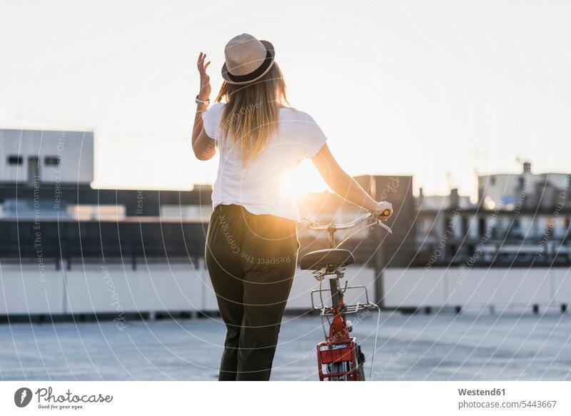 Junge Frau schiebt bei Sonnenuntergang Fahrrad auf Parkebene Sonnenuntergänge schieben anschieben Parkdeck Parkdecks Bikes Fahrräder Räder Rad weiblich Frauen
