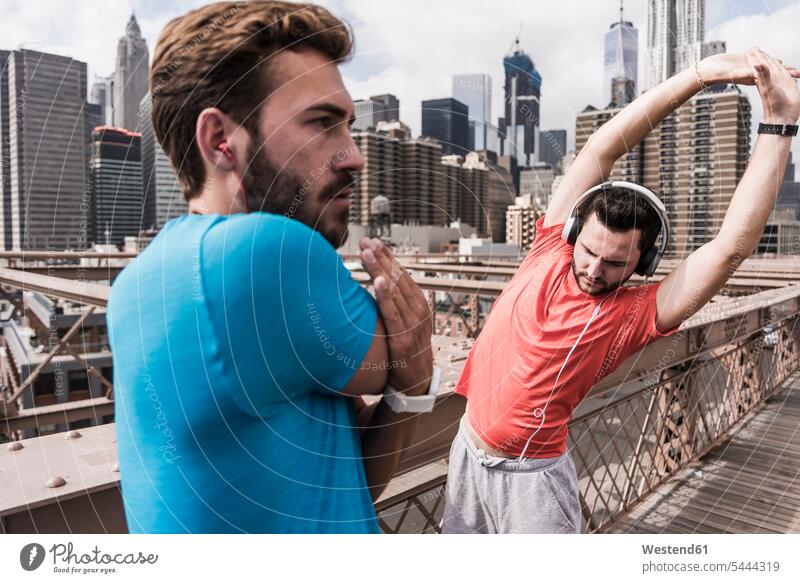 USA, New York City, zwei Athleten strecken sich auf der Brooklyn Brige Freunde Joggen Jogging Mann Männer männlich Brücke Bruecken Brücken dehnen Freundschaft