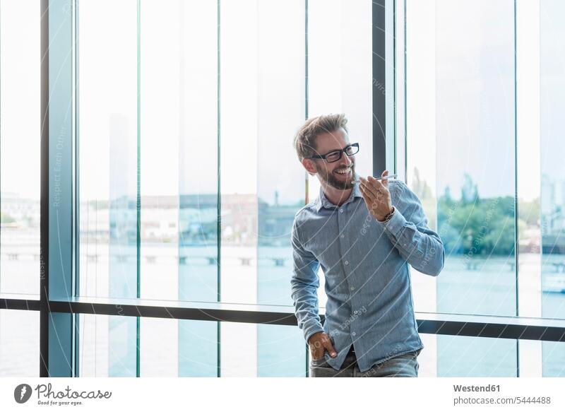 Lächelnder Mann mit Handy am Fenster lächeln Geschäftsmann Businessmann Businessmänner Geschäftsmänner Männer männlich Mobiltelefon Handies Handys Mobiltelefone