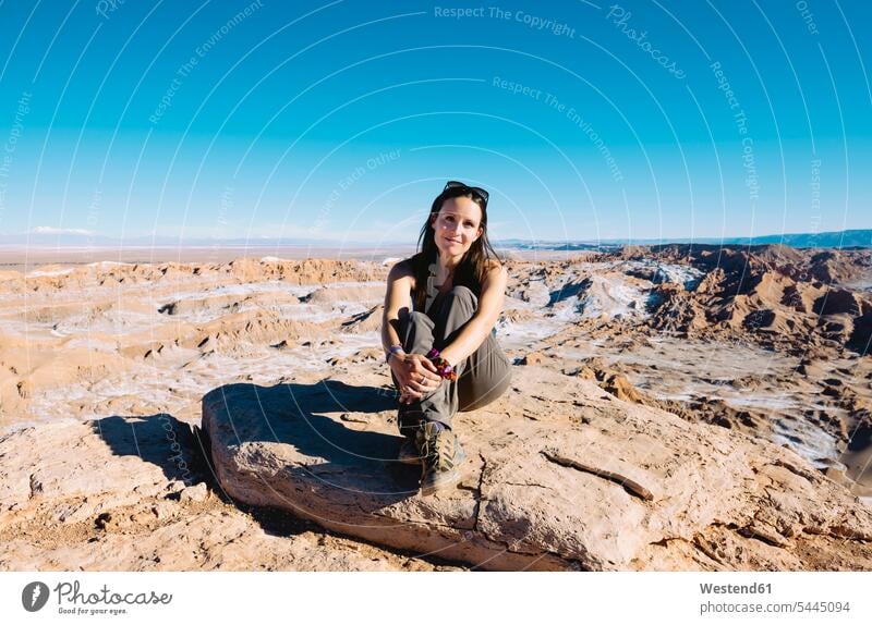 Chile, Atacama-Wüste, lächelnde Frau sitzt im Sonnenlicht auf einem Felsen weiblich Frauen Erwachsener erwachsen Mensch Menschen Leute People Personen sitzen