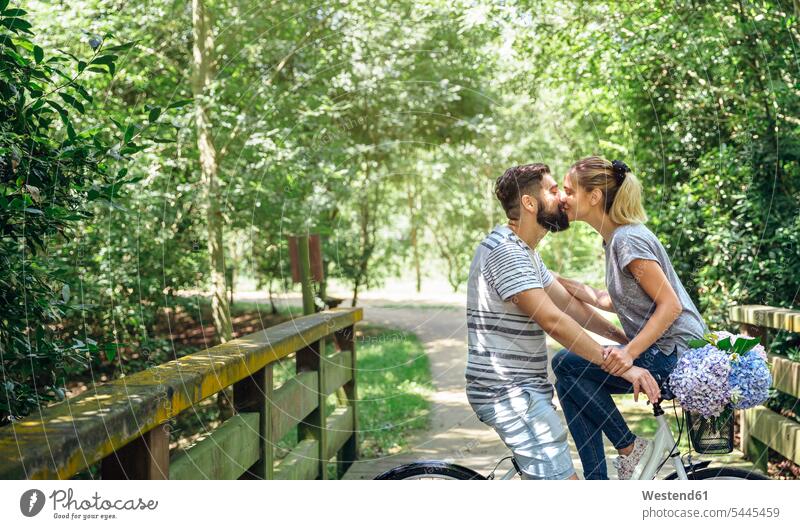 Paar mit Fahrrad küssend auf einem Holzsteg auf dem Land Bikes Fahrräder Räder Rad Weg Wege Pfad Pärchen Paare Partnerschaft ländlich auf dem Lande Küsse Kuss