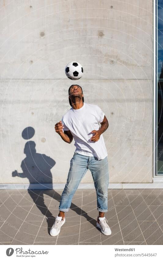 Junger Mann spielt mit Fussball vor einer Betonmauer Fußball Fußbälle spielen Männer männlich Ball Bälle Erwachsener erwachsen Mensch Menschen Leute People