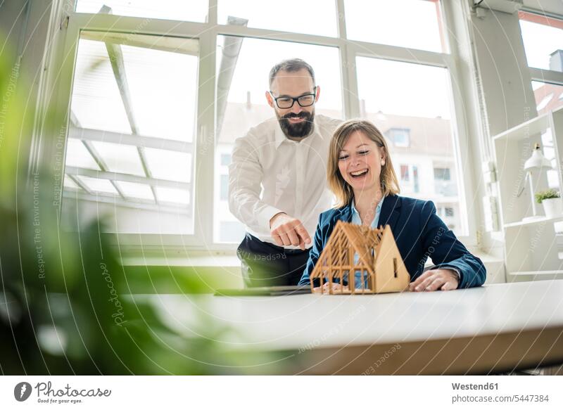 Lachende Frau und lachender Mann mit Hausmodell im Amt Geschäftsfrau Geschäftsfrauen Businesswomen Businessfrauen Businesswoman Büro Office Büros Geschäftsmann