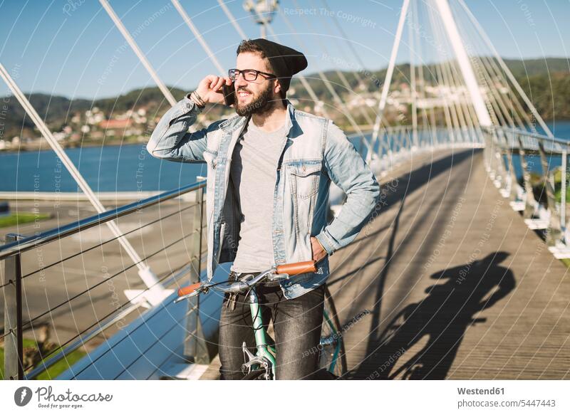 Junger Mann mit Fixie-Rad auf einer Brücke am Telefon lächeln telefonieren anrufen Anruf telephonieren Fahrrad Bikes Fahrräder Räder Handy Mobiltelefon Handies