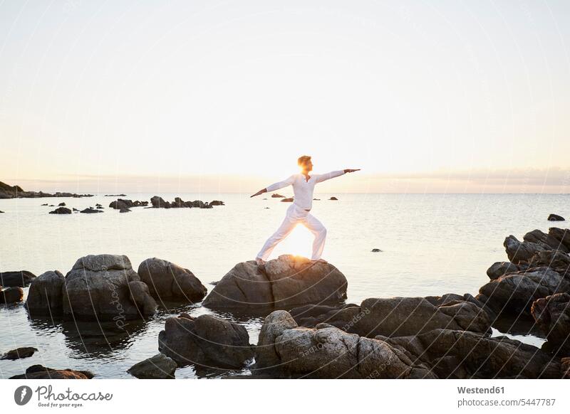 Reifer Mann macht Yoga-Übungen auf einem Felsen am Meer Männer männlich Yogauebungen Yogaübungen Jogauebung Jogauebungen Meere Erwachsener erwachsen Mensch