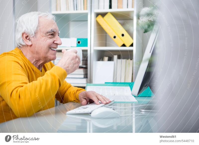 Älterer Mann arbeitet am Computer mit einer Tasse Kaffee sitzen sitzend sitzt arbeiten Arbeit trinken Rechner Männer männlich Senior ältere Männer älterer Mann