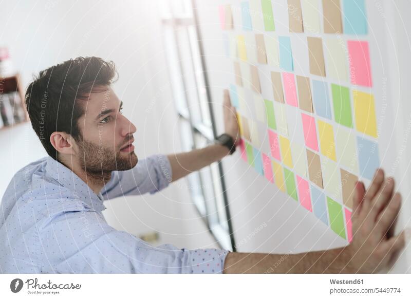 Junger Geschäftsmann arbeitet im Büro mit Haftnotizen an der Wand Strategie Strategisch Brainstorming Ideenfindung schreiben aufschreiben notieren schreibend