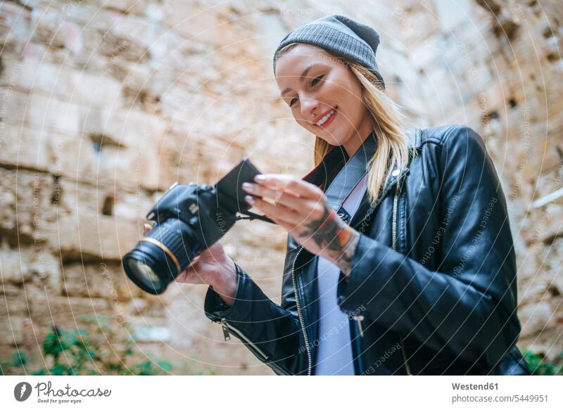 Lächelnde junge Frau betrachtet Fotos auf ihrer Kamera weiblich Frauen Kameras Erwachsener erwachsen Mensch Menschen Leute People Personen Fotoapparat