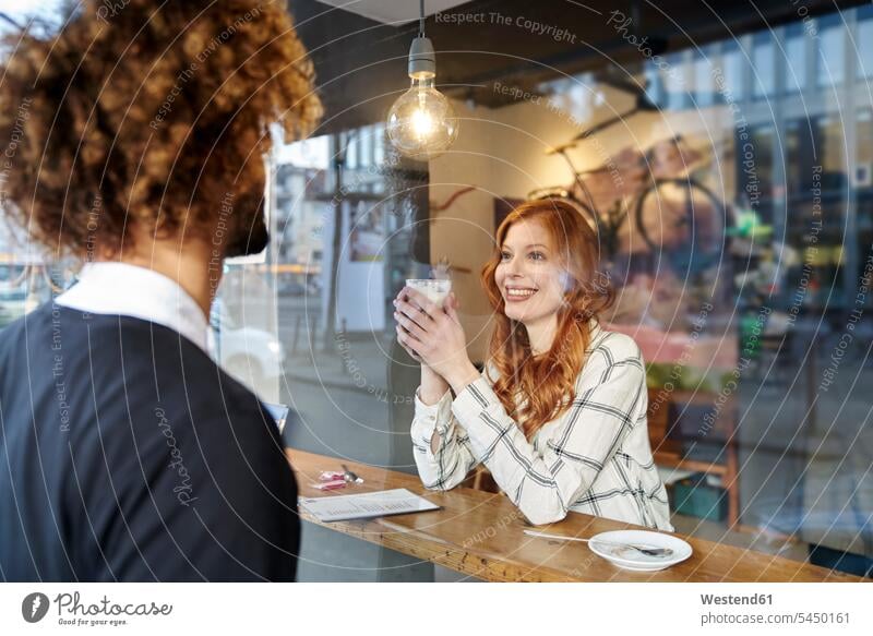 Mann sieht lächelnde junge Frau in einem Café an Cafe Kaffeehaus Bistro Cafes Cafés Kaffeehäuser Paar Pärchen Paare Partnerschaft Fenster Gastronomie Mensch