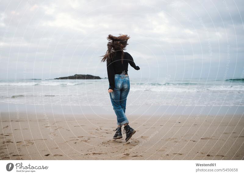 Rückenansicht einer jungen Frau, die auf den Strand springt weiblich Frauen Beach Straende Strände Beaches Erwachsener erwachsen Mensch Menschen Leute People