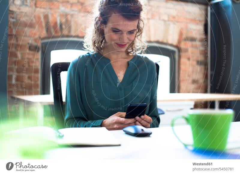 Junge Frau, die mit ihrem Handy am Schreibtisch im Büro telefoniert arbeiten Arbeit Mobiltelefon Handies Handys Mobiltelefone Office Büros Telefon telefonieren