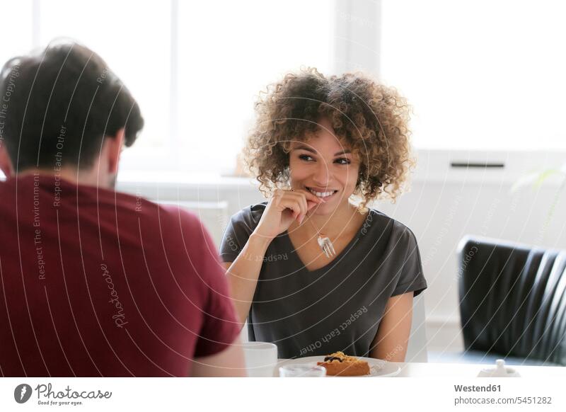 Lächelnde junge Frau isst Kuchen am Tisch und schaut den Mann an Tische ansehen lächeln Paar Pärchen Paare Partnerschaft Zuhause zu Hause daheim weiblich Frauen