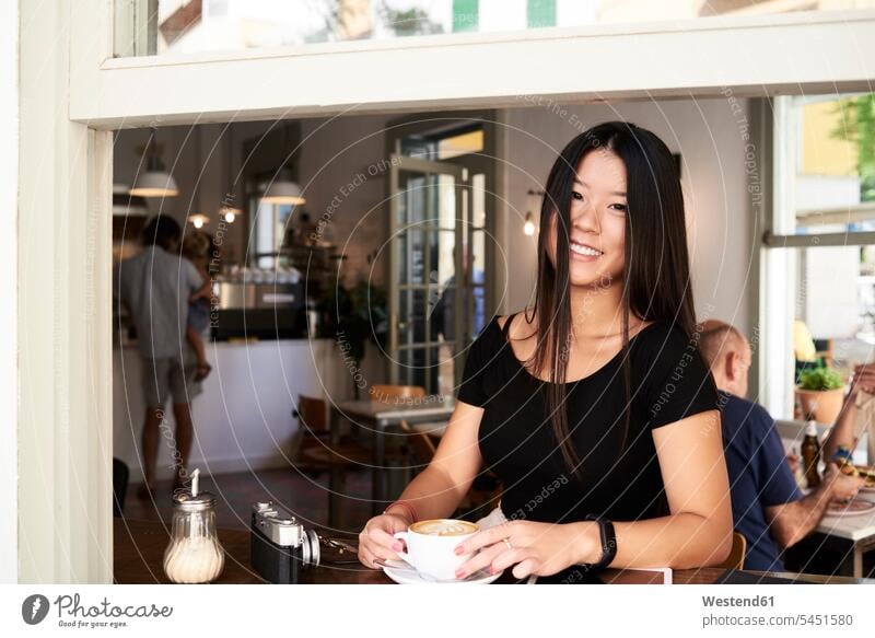 Glückliche asiatische Frau in einem Kaffeehaus neben dem Fenster Asiatin Asiatinnen asiatisches asiatischer weiblich Frauen trinken Cafe Bistro Cafes Café Cafés