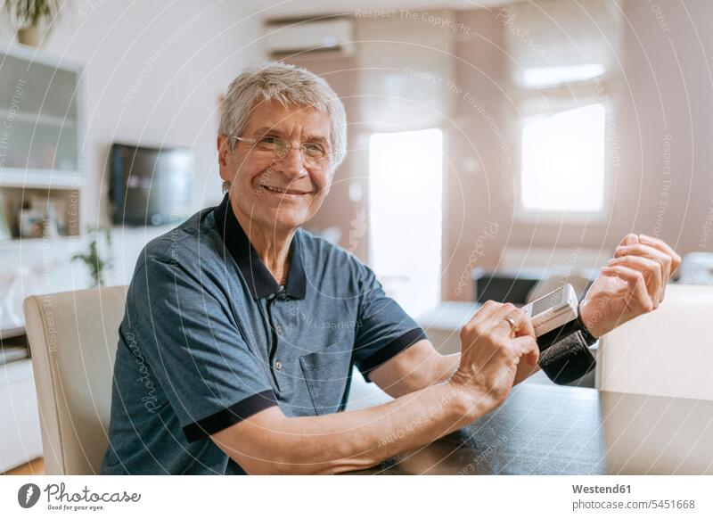 Lächelnder älterer Mann misst seinen Blutdruck prüfen Kontrolle Untersuchung kontrollieren pruefen Senior ältere Männer Senioren männlich lächeln Erwachsener