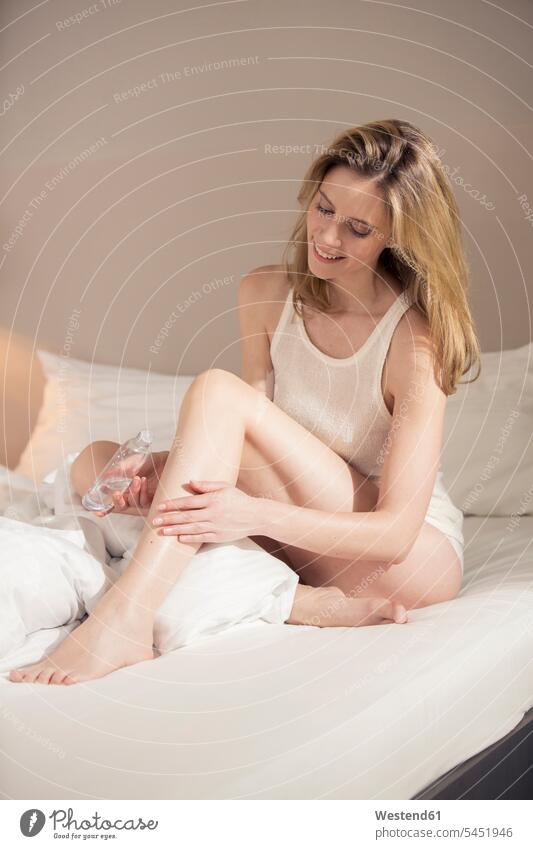 Lächelnde Frau im Bett beim Auftragen von Hautöl Betten lächeln weiblich Frauen Hautoel Hautöle Hautoele Erwachsener erwachsen Mensch Menschen Leute People