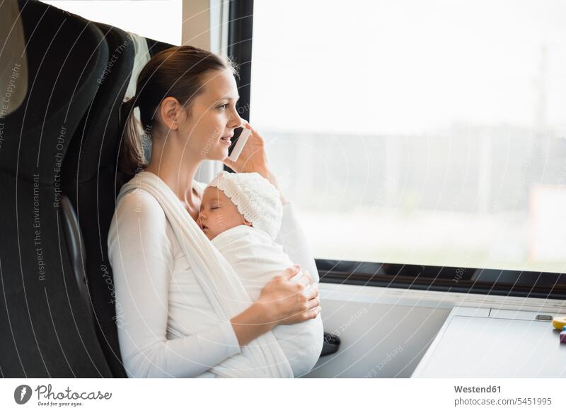 Mutter mit Baby Mädchen reist mit dem Zug und telefoniert mit dem Handy telefonieren anrufen Anruf telephonieren Mobiltelefon Handies Handys Mobiltelefone