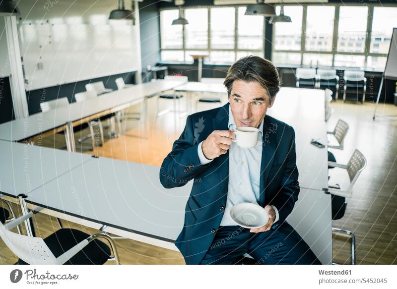 Geschäftsmann mit Tasse Kaffee auf dem Tisch im Besprechungsraum eines Büros sitzend Tische Office sitzt Businessmann Businessmänner Geschäftsmänner