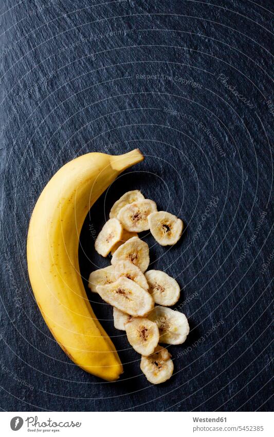 Bananen und Bananenchips auf Schiefertafel schwarzer Hintergrund getrocknet getrocknete getrocknetes getrockneter Frische frisch Gesunde Ernährung Ernaehrung