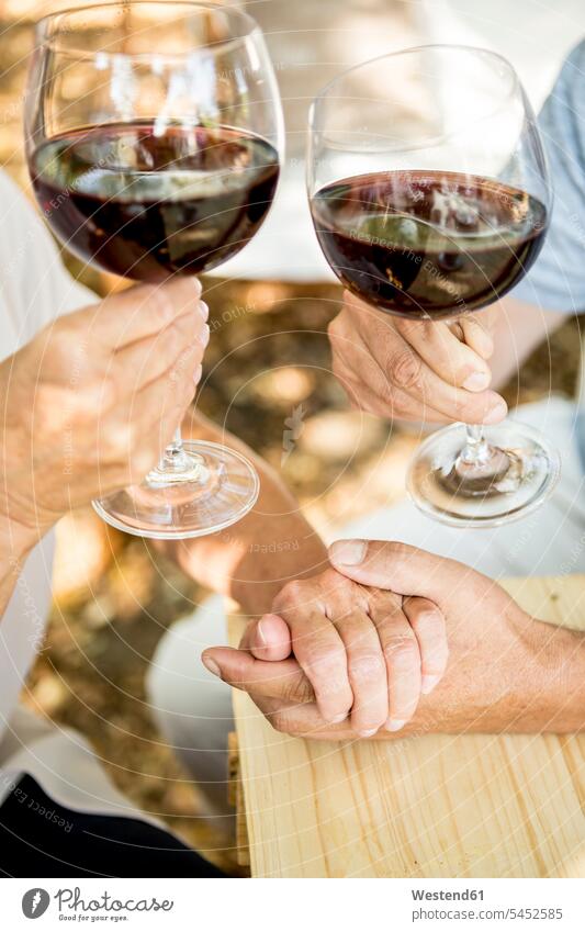 Nahaufnahme eines älteren Ehepaares bei einem Glas Rotwein und Händchenhalten im Freien Hand Hände Paar Pärchen Paare Partnerschaft Wein Weine Mensch Menschen