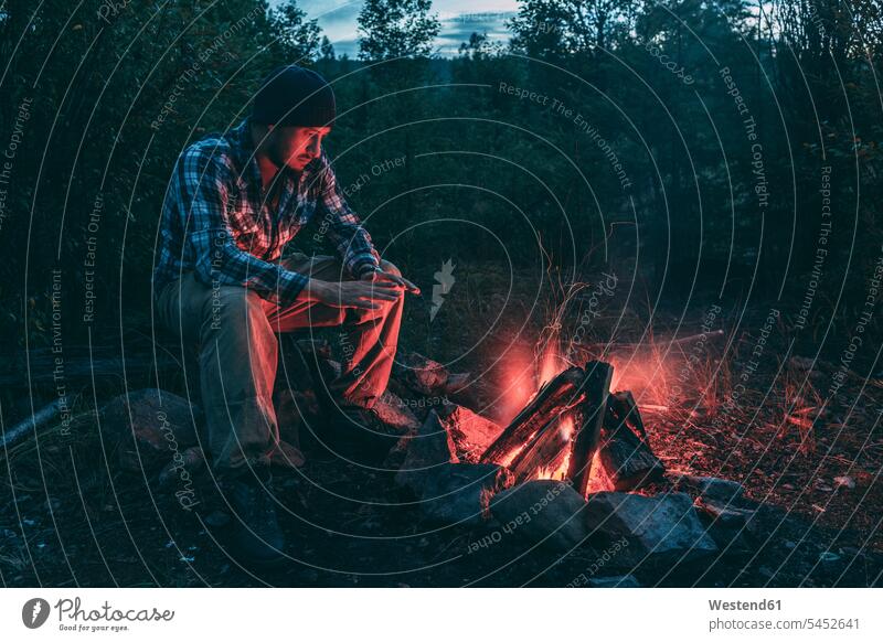 Mann sitzt am Lagerfeuer in ländlicher Landschaft Männer männlich sitzen sitzend Feuer Erwachsener erwachsen Mensch Menschen Leute People Personen Natur