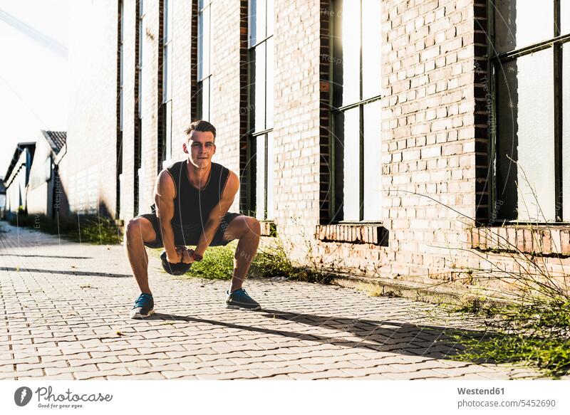 Junger Mann trainiert mit einer Kesselglocke Männer männlich sportlich fit Rundgewicht Kettlebell Kugelhantel Kettlebells trainieren Sportler heben Erwachsener