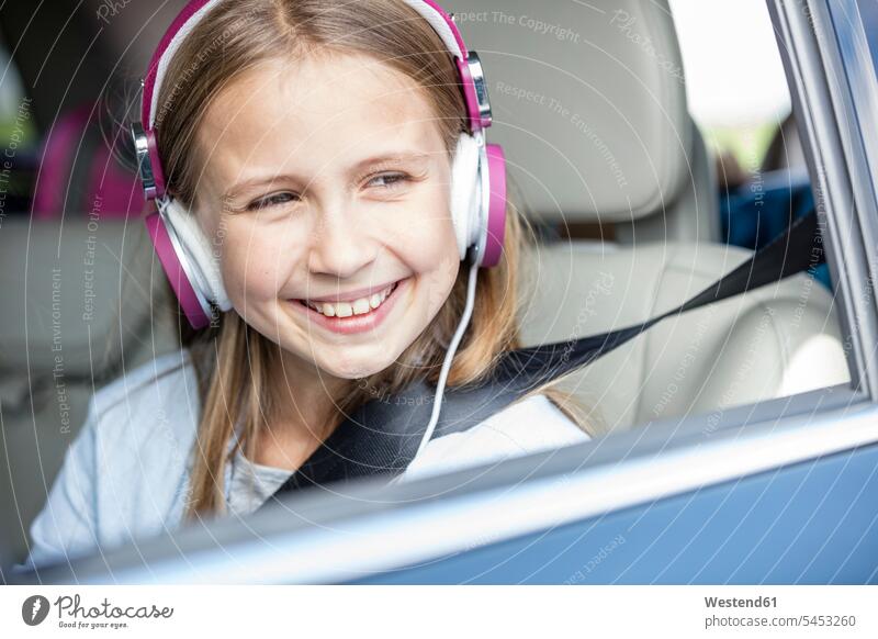 Mädchen sitzt im Auto, schaut aus dem Fenster und hört Musik sitzen sitzend Wagen PKWs Automobil Autos aus dem Fenster sehen durchs Fenster schauen