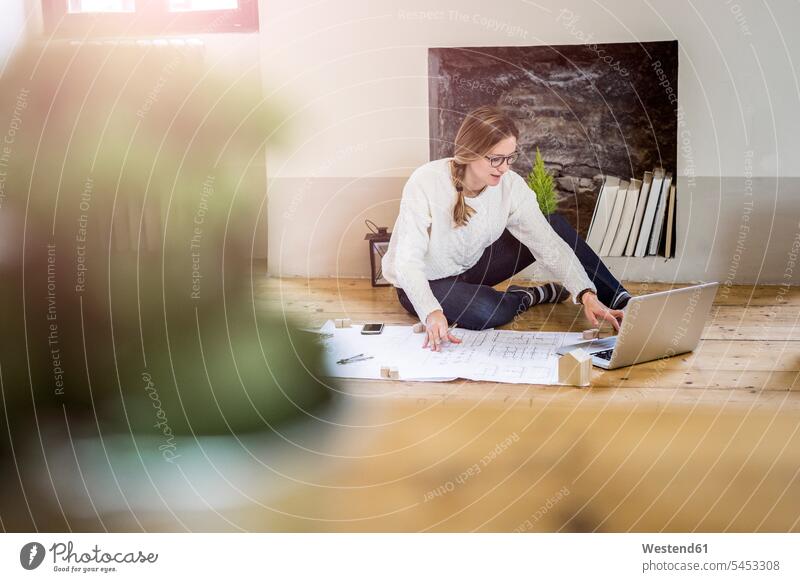 Auf dem Boden sitzende Frau mit Blaupause und Laptop Böden Boeden sitzt weiblich Frauen Notebook Laptops Notebooks Bauplan Architekturplan Konstruktionsplan