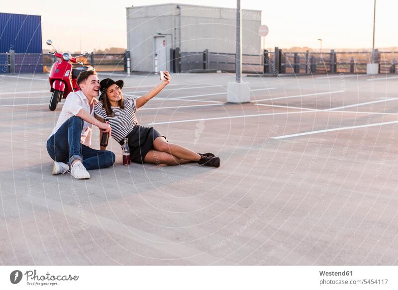 Glückliches junges Paar mit Motorroller auf einem Parkdeck, das ein Selfie macht glücklich glücklich sein glücklichsein Parkdecks Roller Piaggio Pärchen Paare