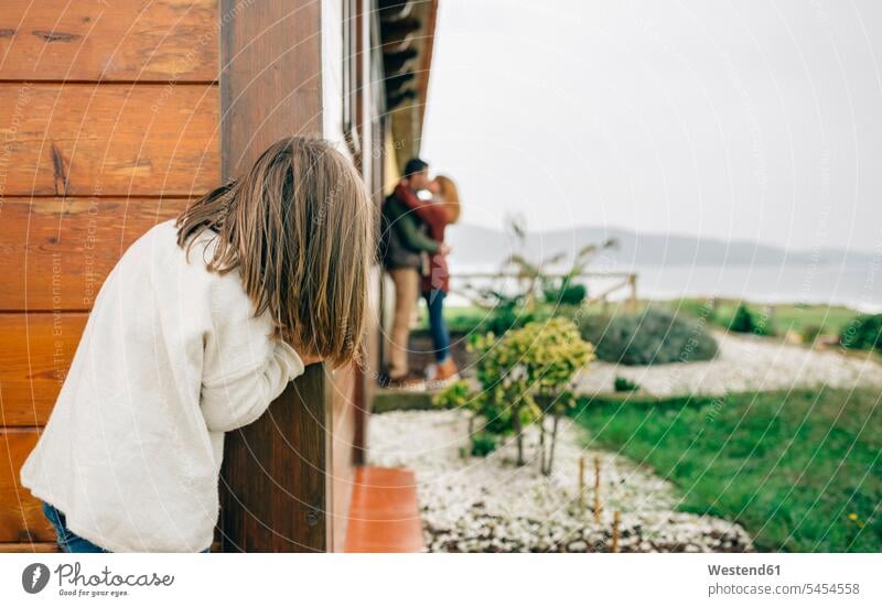 Rückenansicht eines kleinen spionierenden verliebten Mädchens, das sich neben einem Holzhaus küsst Eltern beobachten zuschauen ansehen Familie Familien Mensch