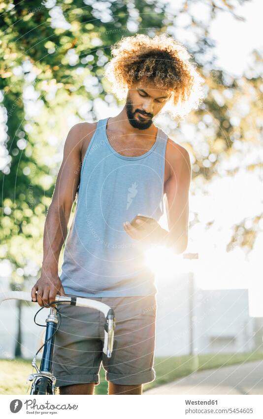 Junger Mann mit Fahrrad überprüft Handy Bikes Fahrräder Räder Rad Mobiltelefon Handies Handys Mobiltelefone Männer männlich Raeder Telefon telefonieren