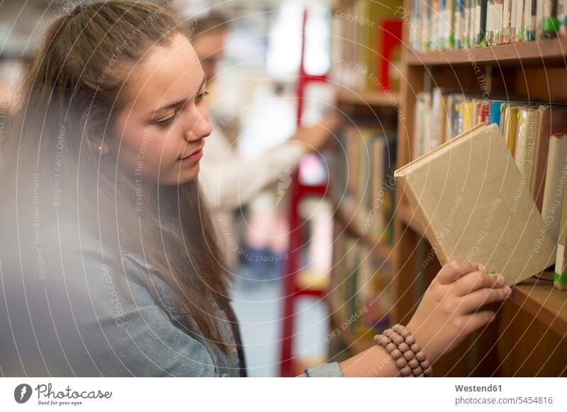 Studentin in der Bibliothek stellt Buch ins Bücherregal zurück Bücherei Schüler Schülerin Schuelerin Schülerinnen Schuelerinnen Bildung Ausbildung lernen Schule