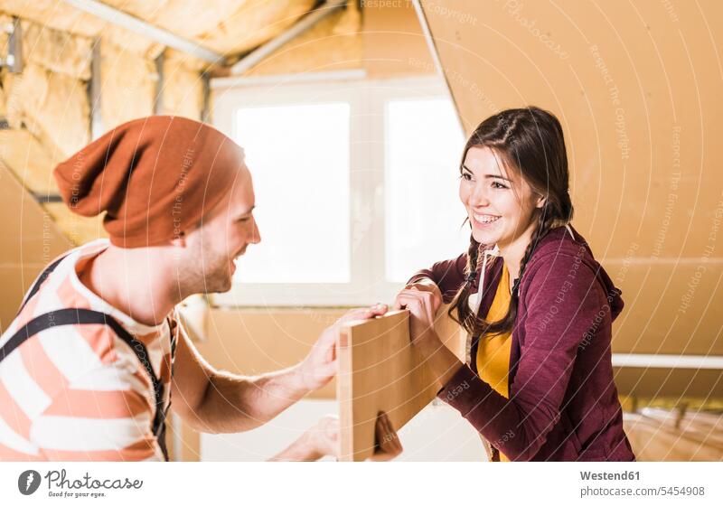 Junger Mann und Frau renovieren ihr neues Haus, halten ein Brett Renovierung Heimwerken Do-it-Yourself DIY Paar Pärchen Paare Partnerschaft schreinern Eigenheim