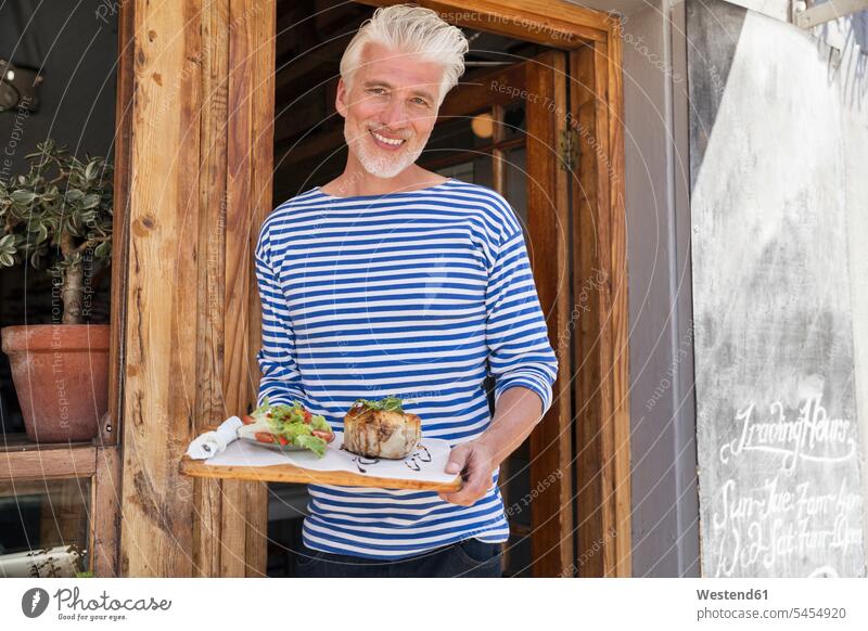 Ein reifer Mann steht vor seinem Restaurant und serviert ein Gericht Tür Türen Besitzer stehen stehend Männer männlich Lokal Speiserestaurant Lokale