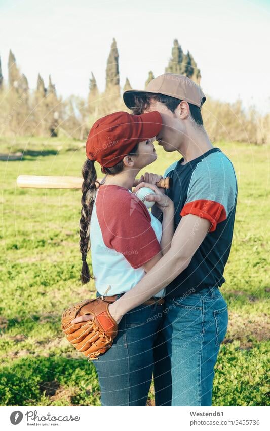 Junges Paar mit Baseballausrüstung küsst sich im Park Baseballspiel Baseballspieler Baseballer Pärchen Paare Partnerschaft küssen Küsse Kuss Sport Mensch