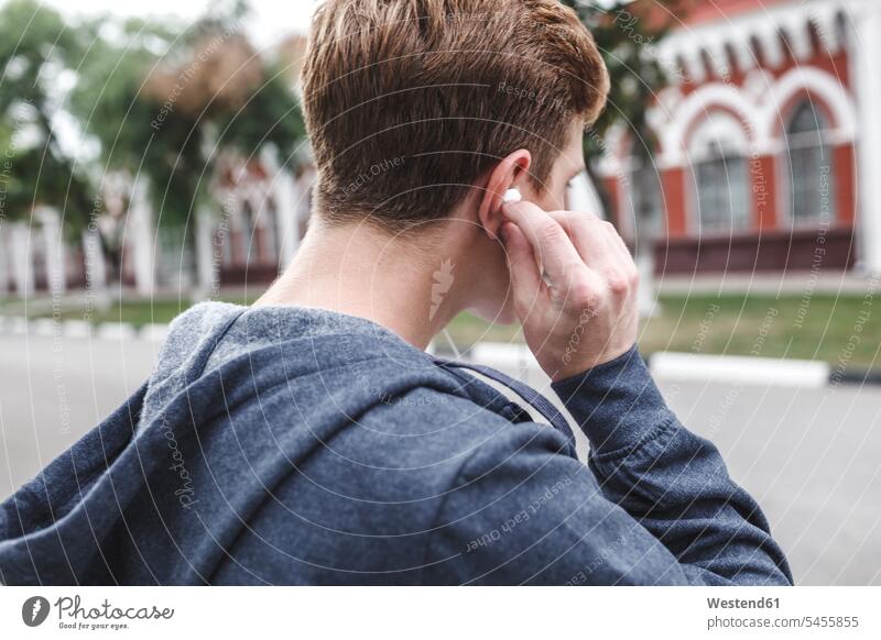 Junger Mann legt Kopfhörer auf hören hoeren Männer männlich Ohrhörer Erwachsener erwachsen Mensch Menschen Leute People Personen In-Ear Kopfhoerer Europäer