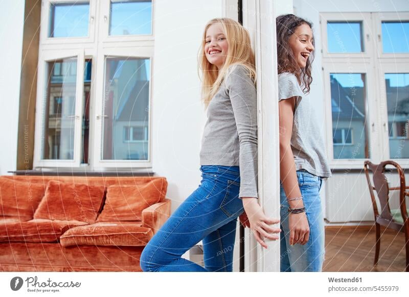 Zwei glückliche Mädchen, die auf gegenüberliegenden Seiten einer Tür stehen weiblich Freundinnen lächeln Glück glücklich sein glücklichsein Kind Kinder Kids