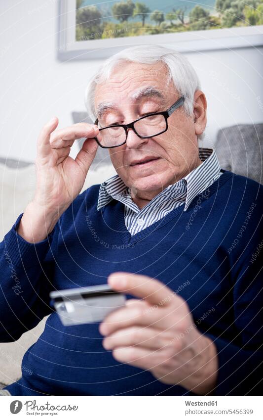 Älterer Mann überprüft seine Kreditkarte EC-Karte Kreditkarten Männer männlich bezahlen sitzen sitzend sitzt Senior ältere Männer älterer Mann Senioren