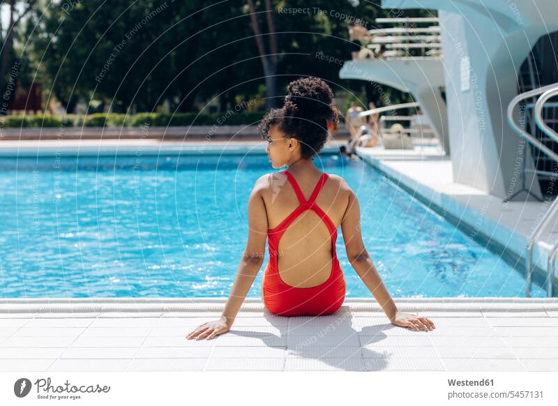 Rückenansicht einer jungen Frau im roten Badeanzug am Poolufer sitzend Fliesen Kachel Kacheln Badebekleidung Badeanzuege Badeanzüge entspannen relaxen sitzt
